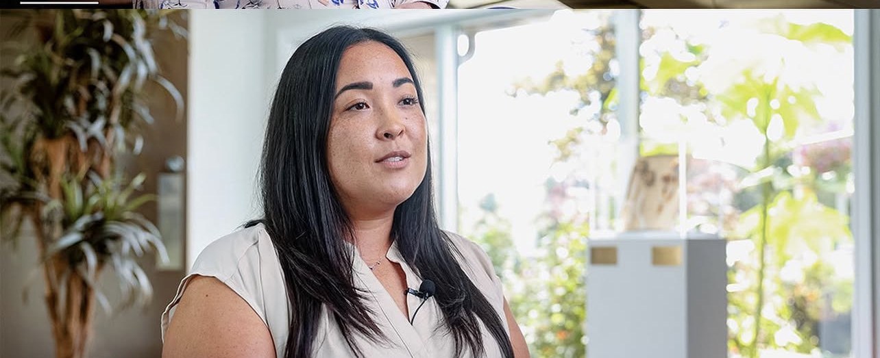 A woman interviewed by tall windows.